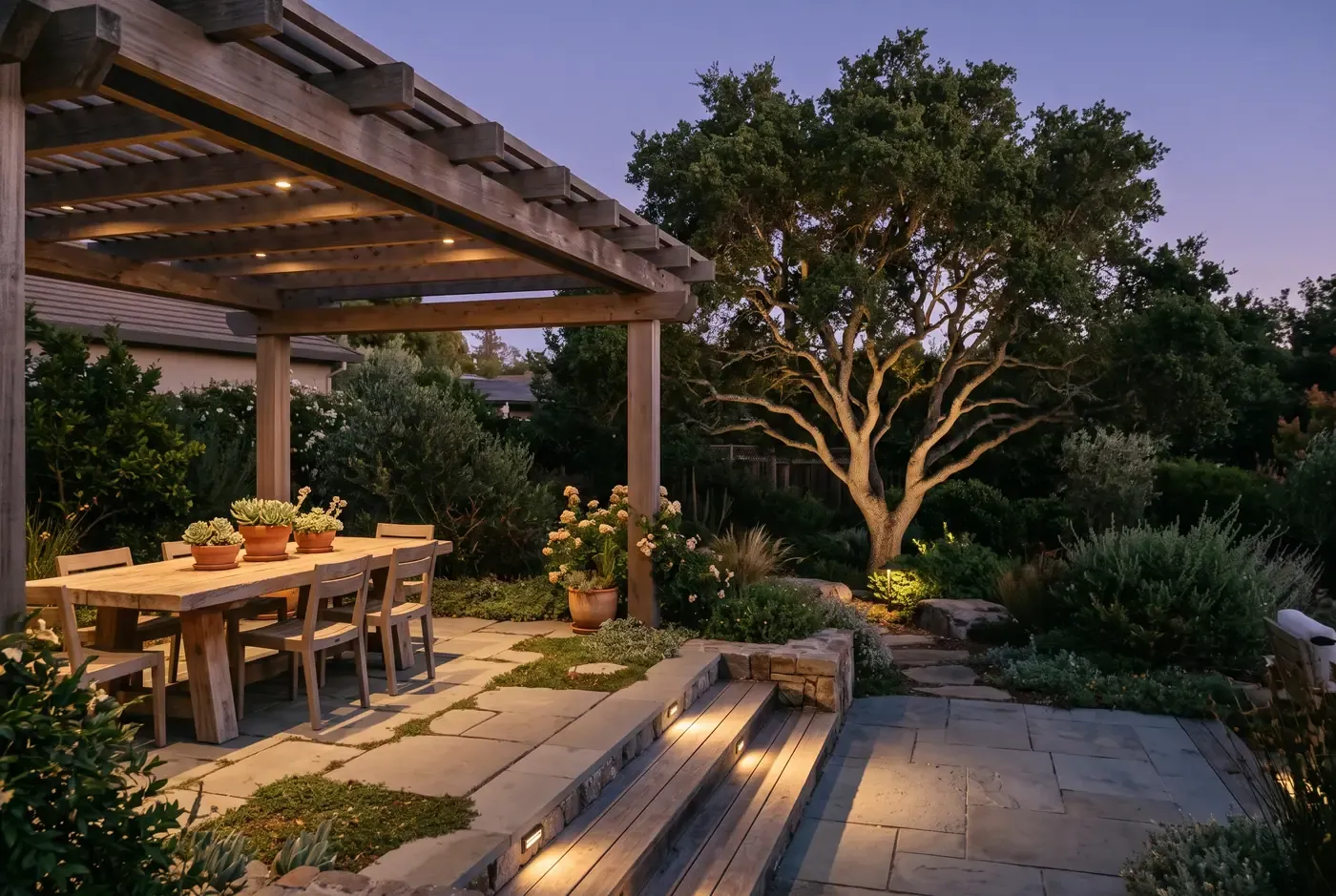 Layered lighting scene: pergola downlights, step lights on stairs, tree uplight, and path markers all with warm 2700K illumination